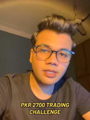 A man with glasses is centered in the shot. The background is a softly lit room with a ceiling light and a ceiling fan visible. The image is well-lit and the overall aesthetic is casual.