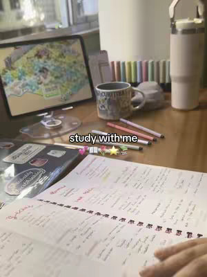 The image shows a study setup. A tablet displaying a map is on the left. A mug, pens, pencils, and a notepad are in focus. The overall composition is well-lit and suggests a study environment.