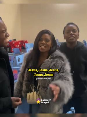 The image captures three individuals indoors. A woman in the center is the focus; she wears a grey, fur-like coat and carries a small beige purse. She is flanked by a man on her left and another woman on her right. The central woman and the man on the left are smiling. In the background and overlaid on the image some text is added, along with a logo in the corner.