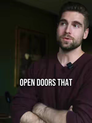 A man with short hair and a beard is centered in an interior shot. Text overlayed on the image states, "OPEN DOORS THAT". The man is wearing a dark red long-sleeve shirt without any strong background elements. The background is a blurry view of a room with a dark green wall with an framed artwork