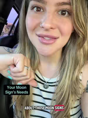 A woman is in a car, speaking while looking towards the camera, with text overlays. She has blonde hair, fair skin, and a nose ring. She is wearing a striped shirt. The text overlays include phrases about moon signs. In the background, a glimpse of trees is visible through the car window. The lighting suggests it might be evening.