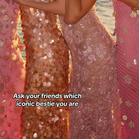 The image shows a close-up of four individuals wearing glittering, sequined dresses. The dresses vary in color from pinks to peach tones, and the figures appear to be standing closely together, possibly hugging. The background seems to be a blurred outdoor scene, likely near water. The lighting is soft and suggestive of a warm setting.