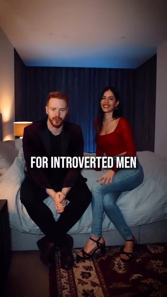 A cover image features a man and a woman in a bedroom setting. The man, with red hair and a beard, is wearing a black shirt and jacket, sitting with his hands clasped. The woman, with long dark hair, is wearing a red top and jeans. Text overlayed reads: 'FOR INTROVERTED MEN'. The background includes a bed, side lamps, and a dark curtain.