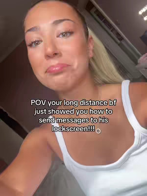 A close-up shot featuring a fair-skinned woman with blonde hair pulled back into a ponytail. She is wearing a white tank top. The text overlay reads 'POV your long distance bf just showed you how to send messages to his lockscreen!!!'