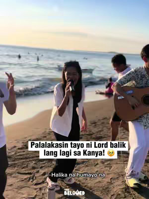 A group of people singing on a beach at sunset.  A woman in the front is holding a microphone and appears to be leading the group. The text overlay says 'Palalakasin tayo ni Lord balik lang lagi sa Kanya!' (roughly translates to 'We will be strengthened by the Lord, just go back to Him')