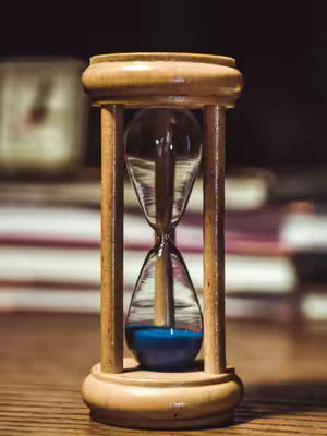 The cover image features a wooden hourglass with blue sand on a wooden surface. The background is blurred, showing books and a clock. The lighting is warm, creating a vintage or nostalgic feel.