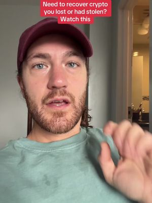 A man with light skin and a beard is the central figure. He's wearing a maroon baseball cap and a light green t-shirt. Text in a red rectangular banner at the top of the image reads: "Need to recover crypto you lost or had stolen? Watch this". The person is looking towards the camera and gesturing with his right hand as if explaining something. The background is a domestic indoor setting with a door frame visible on the right.