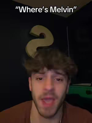A selfie-style video cover image features a young man with light skin and short, tousled brown hair. He is wearing a brown shirt. The background is dark, possibly a wall, with a large, stylized gold question mark on it. Text overlayed at the top says ""Where's Melvin"" in a bold, white font.