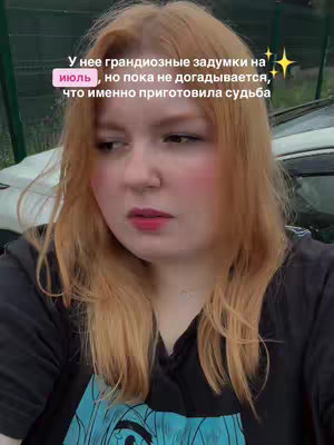 A woman with long auburn hair gazes off-camera with a contemplative expression, her lips gently pursed. She wears a black t-shirt, with a text overlay in the top left corner. The background is slightly blurred green.