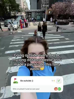 A selfie-style video taken on a city street, showing a woman in the foreground and urban surroundings in the background, including buildings, crosswalks, and pedestrians. Text overlays are present, including motivational phrases.