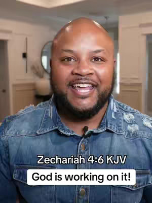 A man with a shaved head and a beard is smiling, looking directly at the camera. He's wearing a denim jacket against a blurred background of a well-lit room. Text overlays are present at the bottom of the image.