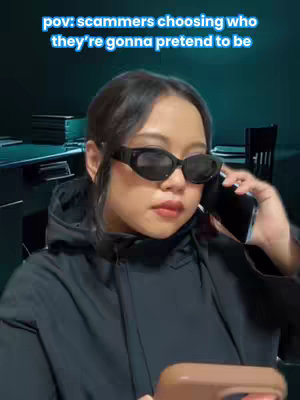 A person wearing sunglasses is holding a phone to their ear and another phone in their other hand. They are in a room that appears to be an office with some visible books.