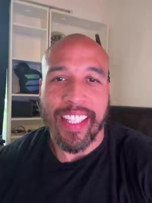 A close-up shot of a man smiling and talking directly to the camera. The background includes a closet or shelving unit.
