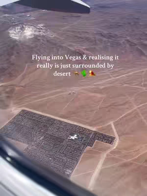 An aerial view from an airplane window showing the Las Vegas cityscape surrounded by a vast desert landscape. Text overlayed on the image reads: 'Flying into Vegas & realising it really is just surrounded by desert'.