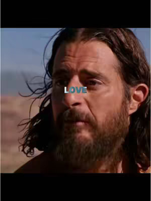 A mid-shot presents a man with dark hair and a full beard. The word 'LOVE' is overlaid on his face in a light color. The background suggests a setting, potentially outdoors, with a muted color palette. The man is looking slightly to the side, creating a contemplative expression, as if deep in thought.