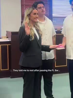 A woman in a black blazer raises her right hand with her palm facing outwards as if taking an oath in a courtroom. Two men stand behind her. The setting appears to be a courtroom.