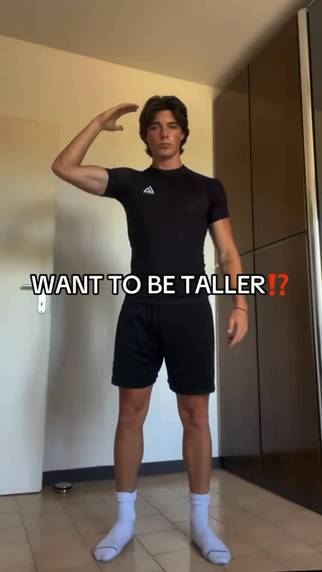 A young man stands indoors, posing with his right arm raised towards his head in a gesture. He wears a black athletic shirt and shorts, white socks and stands on a tiled floor in front of a neutral wall. Text overlayed says, "WANT TO BE TALLER!?"
