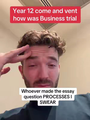 A selfie-style video with a young man looking at the camera. He is touching his forehead and has short, curly brown hair and a beard. Text overlays appear in red at the top and white at the bottom, outlining the main topic of the video.