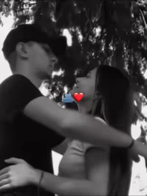 A black and white photo shows a couple embracing, likely outdoors with a blurred tree background. The man, wearing a hat, and the woman are close, with a heart and a symbol of a cloud in the image