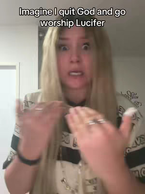 A mid-shot of a woman with long blonde hair, looking directly at the camera with a shocked expression. She's wearing a patterned shirt. Her hands are raised as if in a gesture of surprise or disbelief.