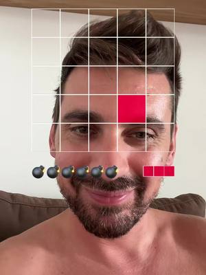 A selfie-style shot featuring a man with a grid overlay, red squares and stylized bomb graphics overlaid on his face. The man faces the camera with a slight smile and a partially nude upper chest.