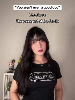 The cover image showcases a young woman against a neutral background. She has long, dark hair with a fringe and is wearing a black t-shirt with a logo. Text overlays are displayed at the top, and there are small figurines and a plant visible in the background.