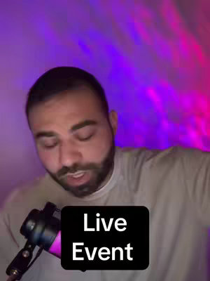A man with a beard and short hair speaks into a microphone overlaid by a black box with white text that reads "Live Event". The background is blurred with purple and pink light.