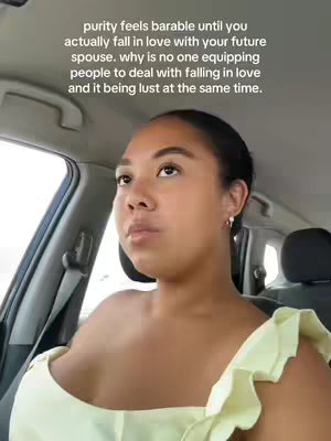 A woman with dark hair looks slightly up and to the right while inside a car. She is wearing a light yellow top and the scene appears to be captured from a low angle, looking upward.