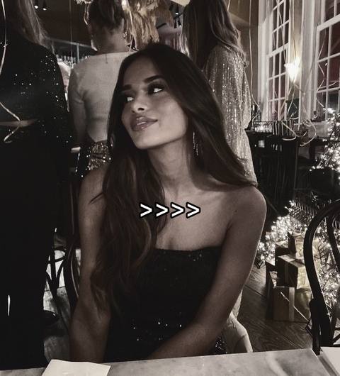 A woman in a black strapless top gazes to her left, with other people and decor in the blurred background. The image has a muted color palette.
