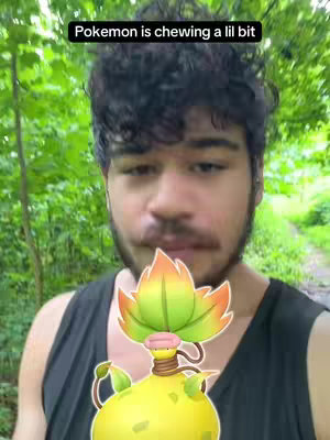 A selfie-style shot featuring a man in front of a blurred green background. Above him is text in a black box reading: 'Pokemon is chewing a lil bit.' In the foreground is a stylized illustration of VictreeBell. The man is looking at the camera directly and has dark curly hair.