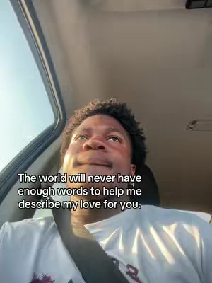 A selfie-style shot taken from inside a car, with the creator's face taking up the majority of the frame. The background shows the car's interior, roof, and sky. The lighting appears to be natural daylight. The creator is wearing a white t-shirt and has short, dark, curly hair. Text is overlaid on the image