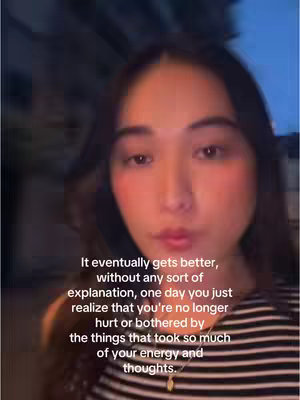 A selfie-style shot featuring a young woman. She appears to be indoors, possibly at night or in a dimly lit setting, as the background is dark and diffused. The woman has long, dark hair. She is wearing a striped black and white top. She has some blush applied to her cheeks. Text overlayed on the image offers a motivational message.