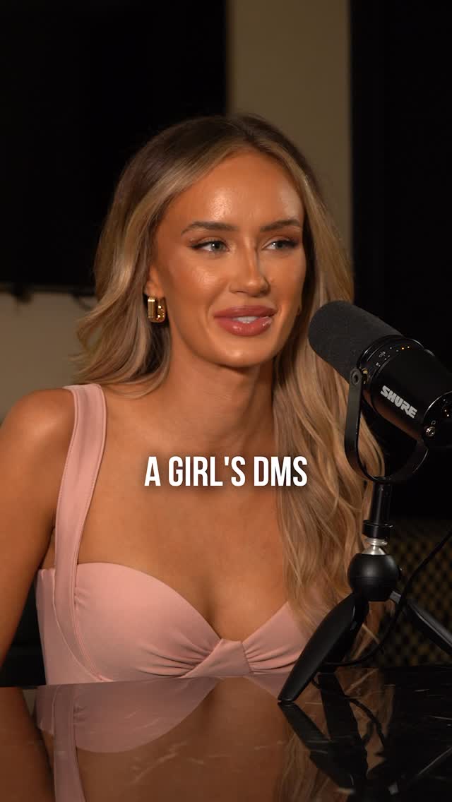 A woman with long blonde hair wearing a pink top and gold earrings is seated in a well-lit room. She's positioned in front of a microphone, seemingly about to speak. Text overlayed reads: A GIRL'S DMS