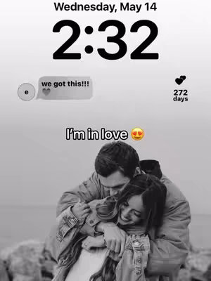 A black and white photo shows a couple embracing. The woman is in the foreground, smiling, with the man hugging her from behind, his face close to hers. The background is blurred, likely a natural setting. The image includes additional elements: a time and date display at the top, a message bubble on the left with a text. The overall composition is intimate and focused on the couple's affection.