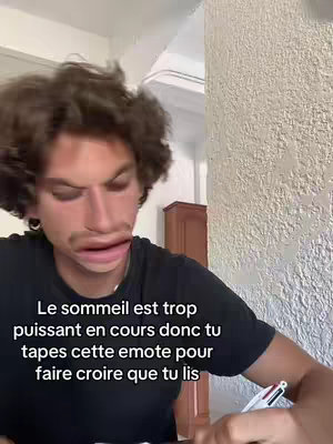 A young man with curly hair and a slight double chin is looking directly at the camera with an exaggerated facial expression due to a filter. He appears to be in a room, with a light-colored wall behind him. Text in French is overlaid on the bottom of the image.