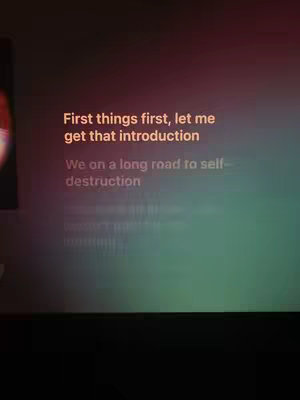 The image shows a screen with orange text over a green and brown gradient background. The text includes song lyrics.