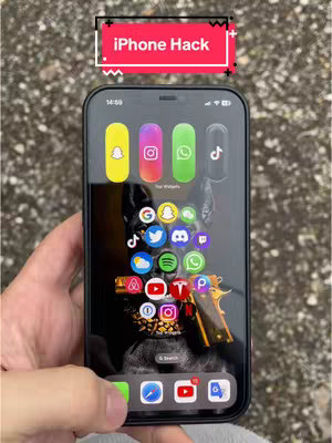 A close-up shot of an iPhone displaying a custom home screen with app icons and widgets, held in front of a gray textured background. The phone's screen has a dark background with several app icons; widgets are arranged vertically. The cover image has the text overlay "iPhone Hack" on a red background.