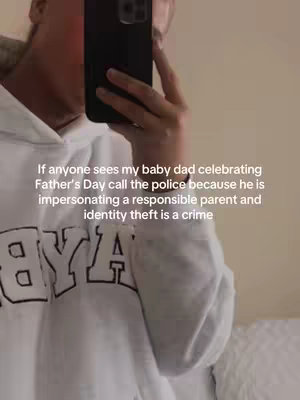 The image appears to be a selfie taken by an individual holding a black phone in front of their face, partially obscuring it. They are inside, evidenced by the plain off-white background, and wearing a white hoodie with 'BYA' in bold, dark lettering. The person's arm holds the phone up to capture the shot. The overlaid text in the image addresses celebrating Father's Day and jokes about identity theft. The overall composition is focused on the person, with the hoodie and text serving as secondary elements. A simple, casual setting with the focus on the subject and text.