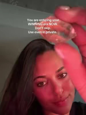 A woman with dark hair and brown eyes is holding a crystal in front of her face, filling the frame. Overlayed text encourages viewers to embrace a 'WINNING era'. The image is bathed in a reddish hue.