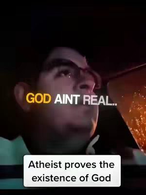 A medium shot of a man with dark hair in a car, looking upwards. The text overlay in large gold letters says "GOD AINT REAL..." with a smaller white box below saying "Atheist proves the existence of God". The background is dark, with hints of orange, potentially indicating taillights or streetlights.