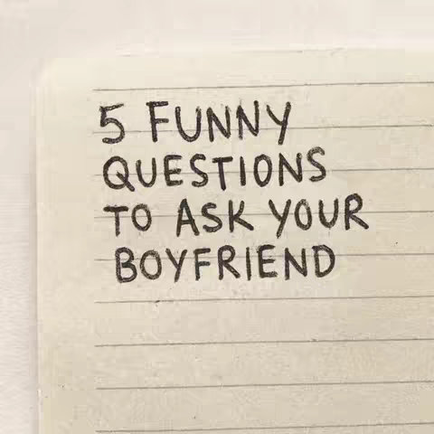 A close-up shot of a notebook page with handwritten text. The page has horizontal lines and a slight texture. The text is in black ink and reads, '5 FUNNY QUESTIONS TO ASK YOUR BOYFRIEND'. The writing is in a casual, slightly uneven style.