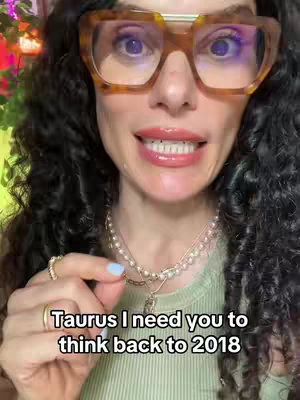 A woman with curly hair and large glasses is facing the camera, smiling and speaking. Text overlay is present at the bottom.