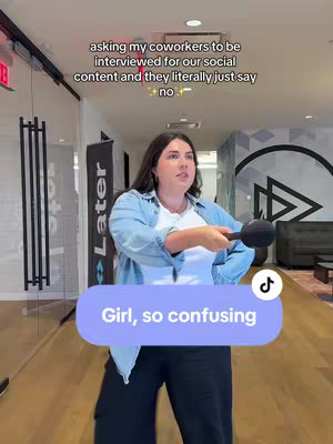 The cover image shows a woman holding a microphone in an office hallway. She's wearing a denim jacket, white top, and black pants. Overlaid on the image is a light purple banner with the text "Girl, so confusing". Above the woman, some text reads, asking my coworkers to be interviewed for our social content and they literally just say no.
