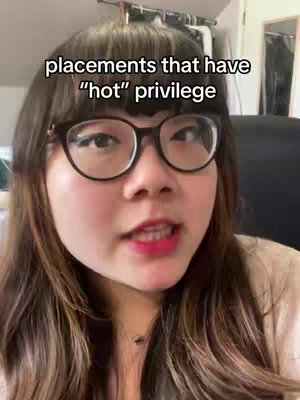 A woman with dark hair and glasses is the focus, framed from the chest up. She is talking, with a close-up shot. Text overlayed at the top reads, "placements that have 'hot' privilege". The background is blurred, suggesting an indoor setting.