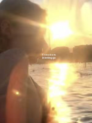 A person's silhouette is seen in soft focus against a bright sunset over a body of water. The light creates a warm, ethereal glow, while a text overlay reads, 'Freedom in letting go.'