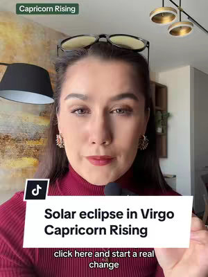 A woman with dark hair and red lipstick centered in the frame. She wears a red turtleneck and has glasses perched on her head. Text overlays read "Capricorn Rising" in a green bar at the top and a white banner at the bottom with the video's title and a call to action.