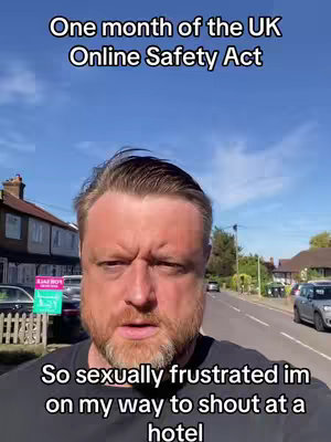 A man with a beard stands on a street with houses in the background and text overlayed in white at the top and bottom of the image..