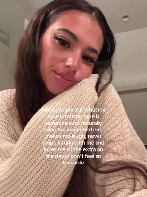 A close-up of a woman with long dark hair, looking slightly down and to the left with a soft expression. She leans her head on her left arm, which is covered by a cream-colored sweater. Text is overlaid on the image.