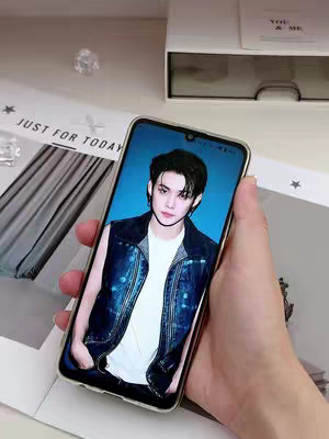 A person is shown holding a smartphone displaying a picture of a man. The background includes part of a white box and some text. The person's hand and arm are also visible.