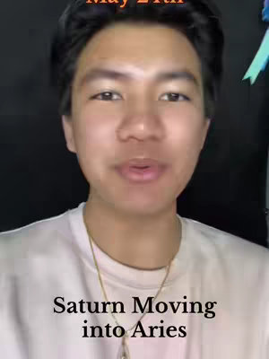 A selfie-style video cover image featuring a young man in a white t-shirt with a gold chain. Text overlays state the date "May 21st" at the top and "Saturn Moving into Aries" near the bottom.